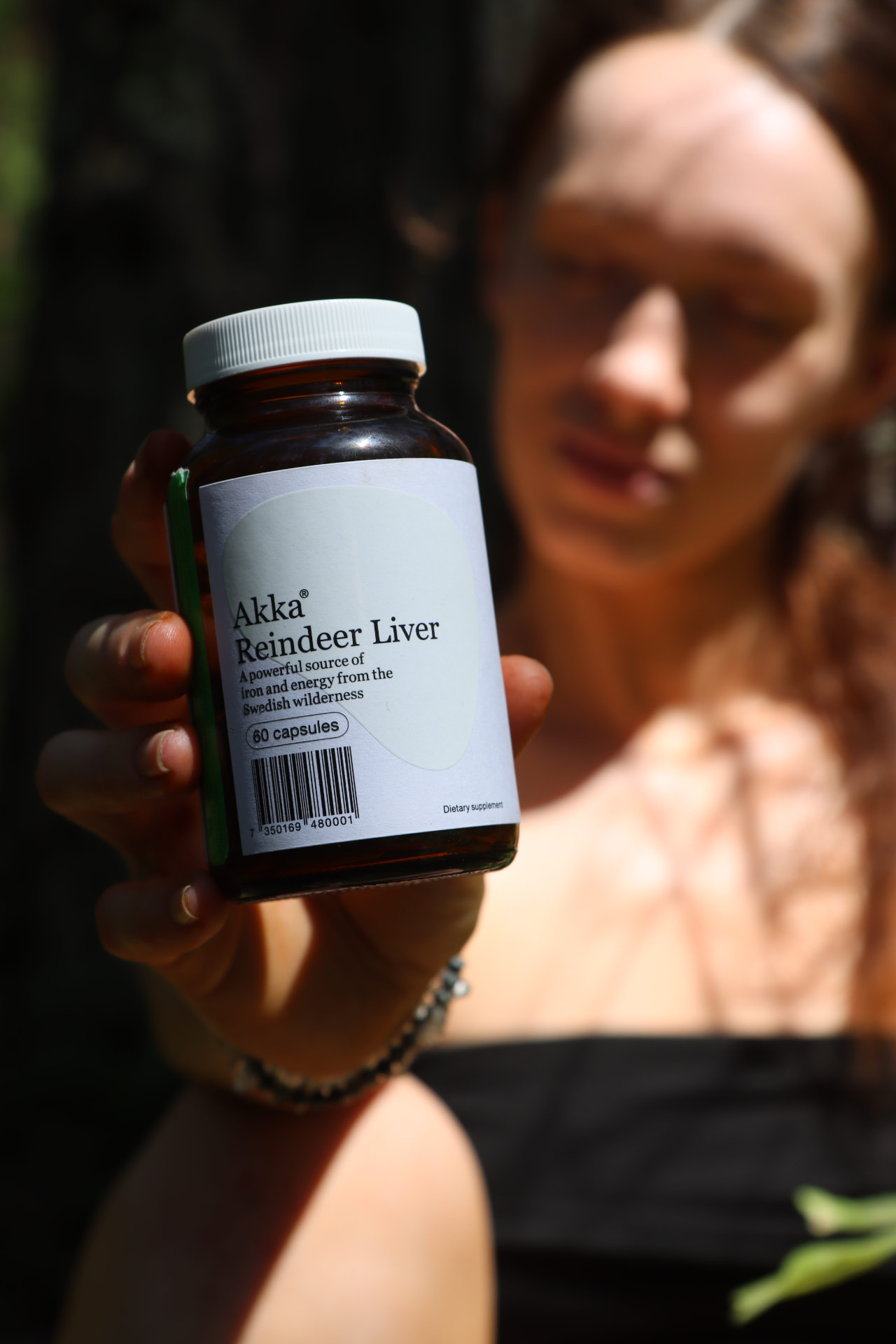 Akka Reindeer Liver bottle held forward with the forest blurred behind