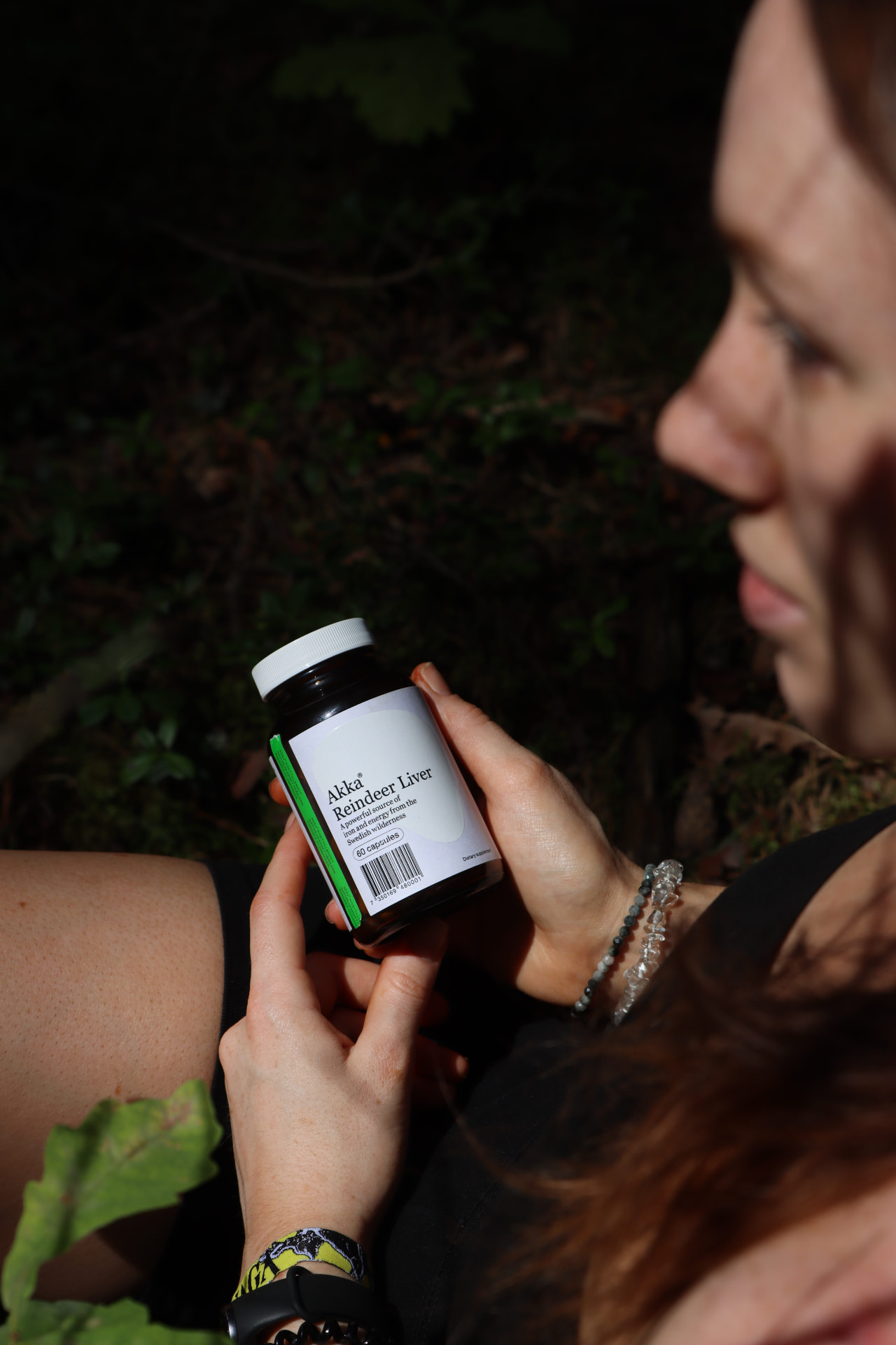 Akka Reindeer Liver bottle held in hand in a sunlit forest
